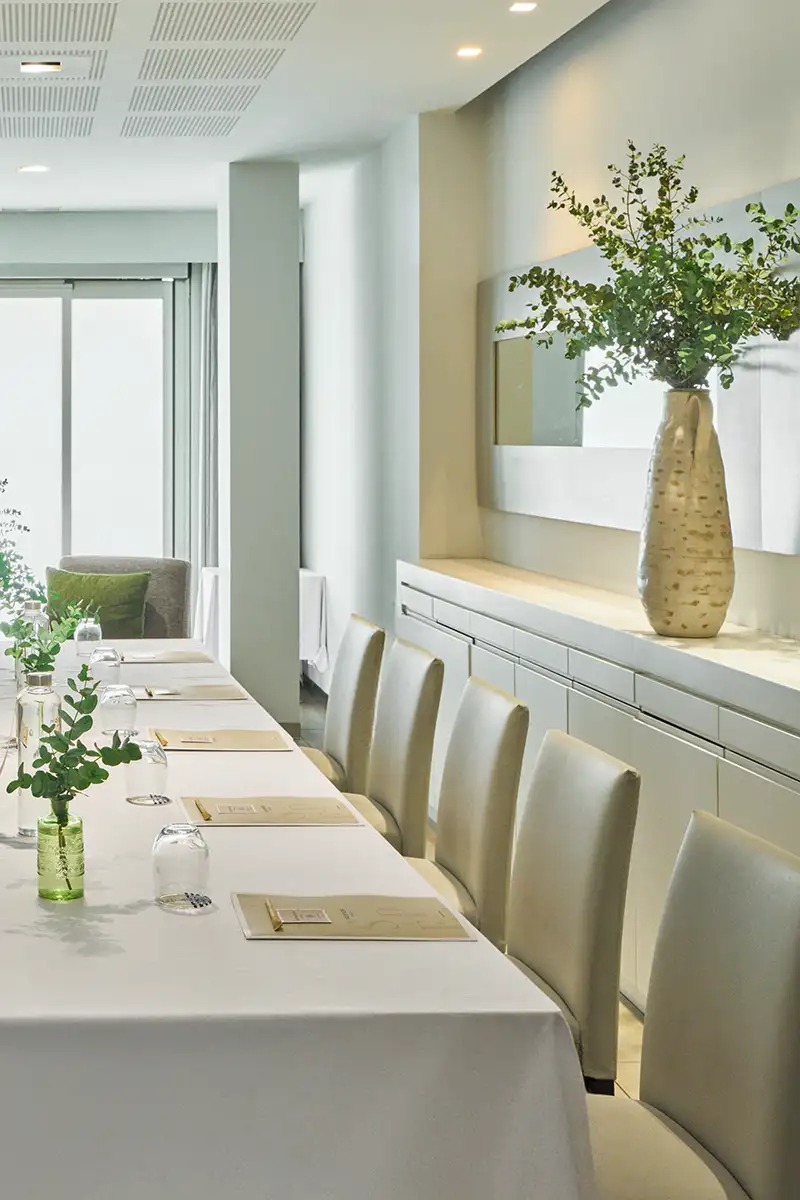 Mesa de comedor moderna con jarr&oacute;n dorado y plantas verdes en interior luminoso