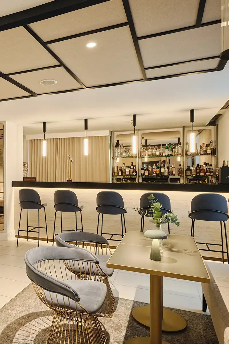 Bar con barra de bebidas, mesas y sillas en un espacio moderno y elegante.