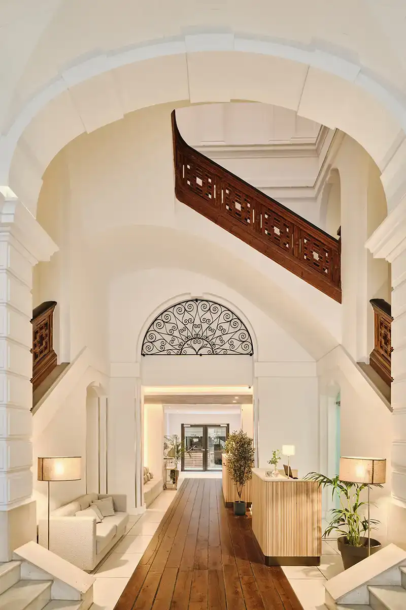 Pasillo interior luminoso con arcos, baranda de madera y l&aacute;mparas.