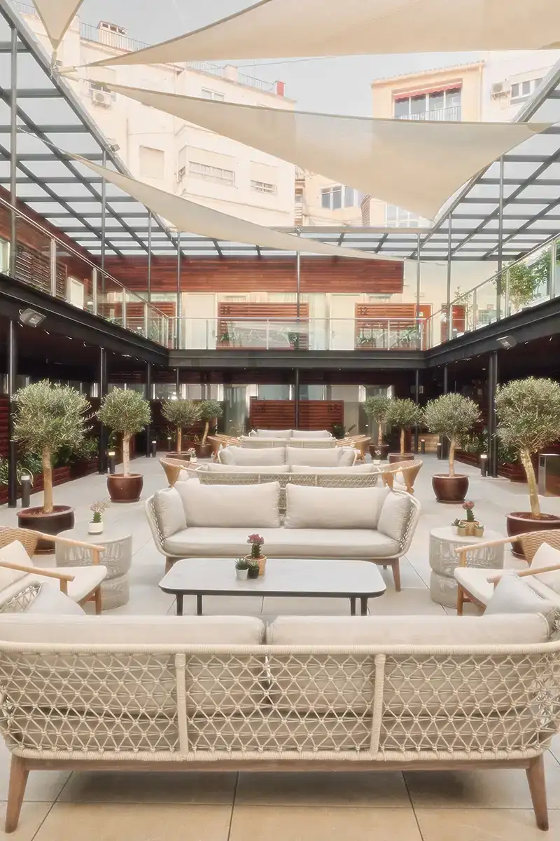 Patio con muebles blancos y cojines, plantas en macetas y techo de lona.