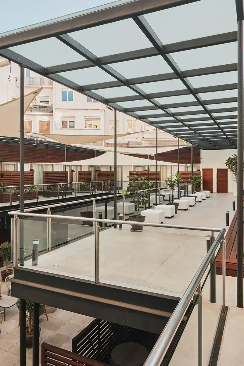 Patio interior moderno con p&eacute;rgola met&aacute;lica, zona de descanso y jardineras