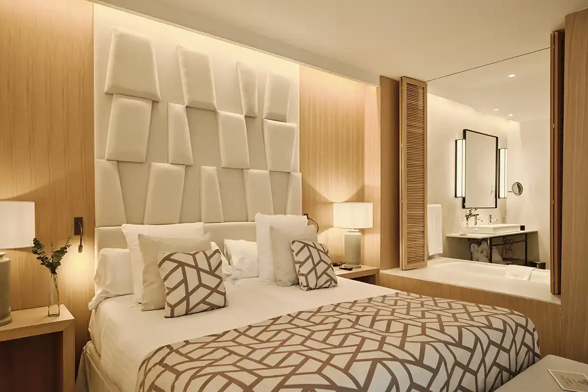 Dormitorio moderno con cama, cabecero 3D, l&aacute;mparas y espejo en ba&ntilde;o integrado