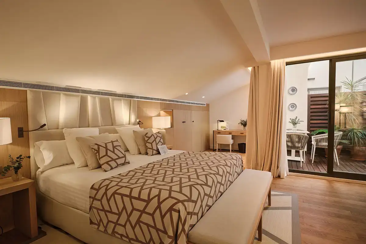 Suite hotelera moderna con cama, cortinas y salida a terraza con jard&iacute;n