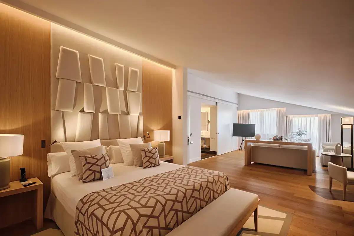 Suite moderna con cama doble, paneles decorativos y zona de sala luminosa