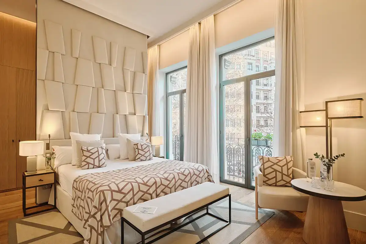 Dormitorio moderno con cama blanca y cortinas junto a grandes ventanales