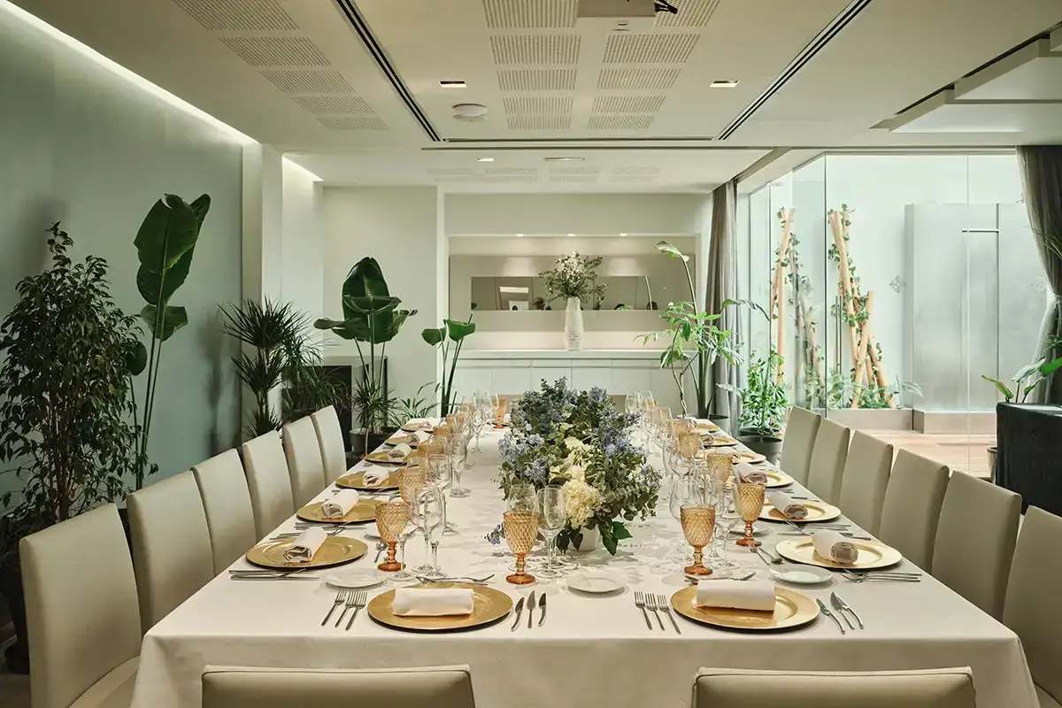 Mesa de banquete con arreglos florales y vajilla en un sal&oacute;n moderno y luminoso