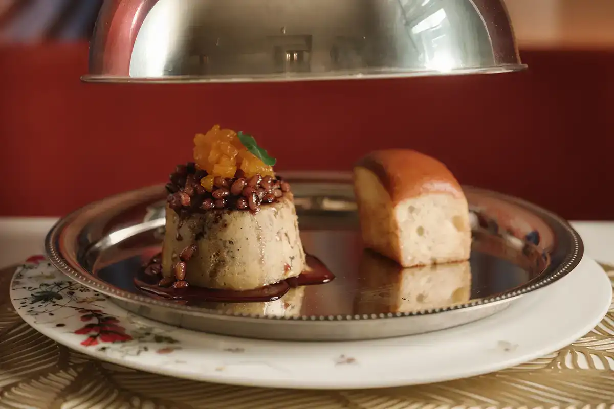Postre servido: bud&iacute;n con salsa oscura y flor de cebolla, en bandeja.