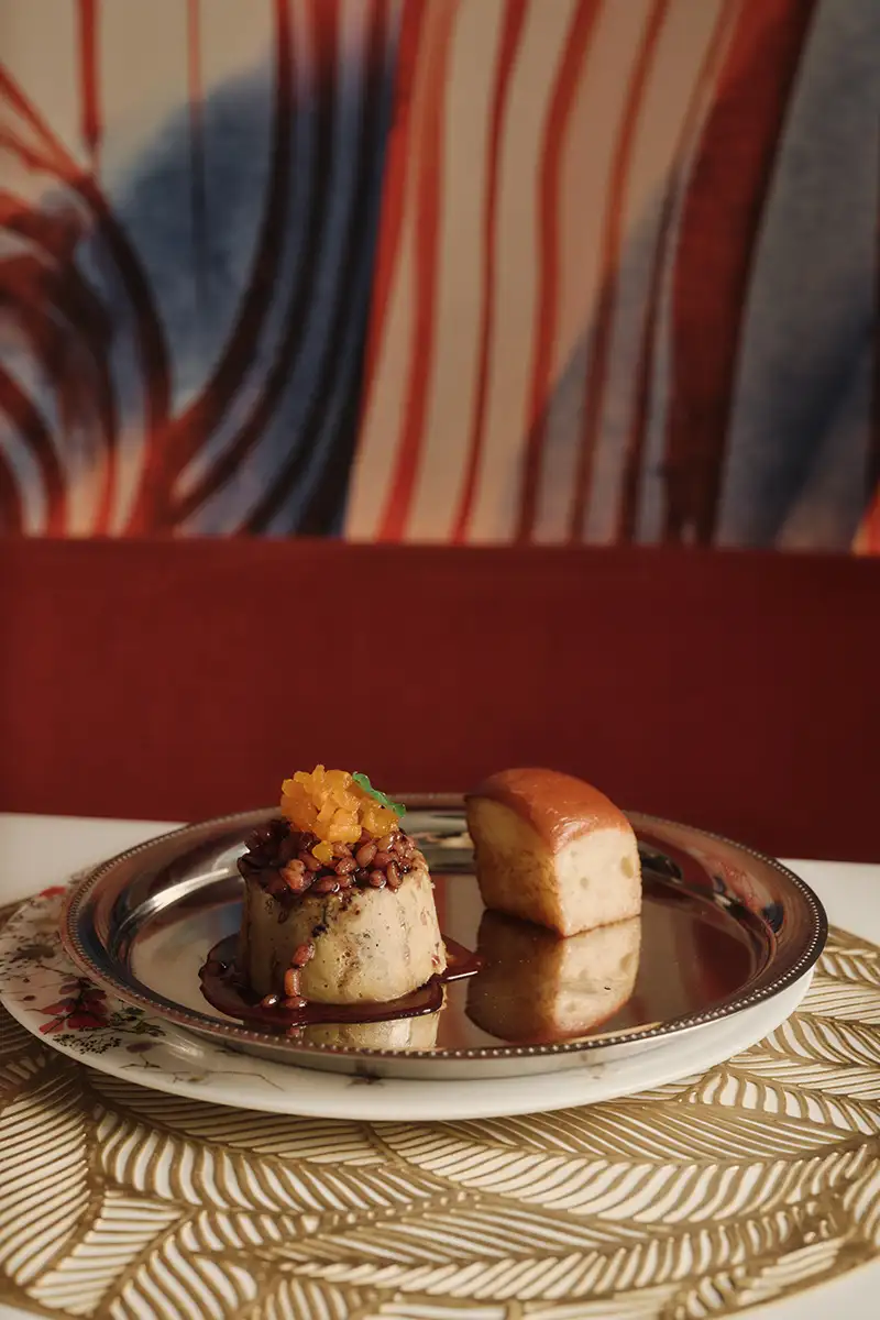 Postre en plato met&aacute;lico con trozos, sobre fondo rayado y manteler&iacute;a decorativa