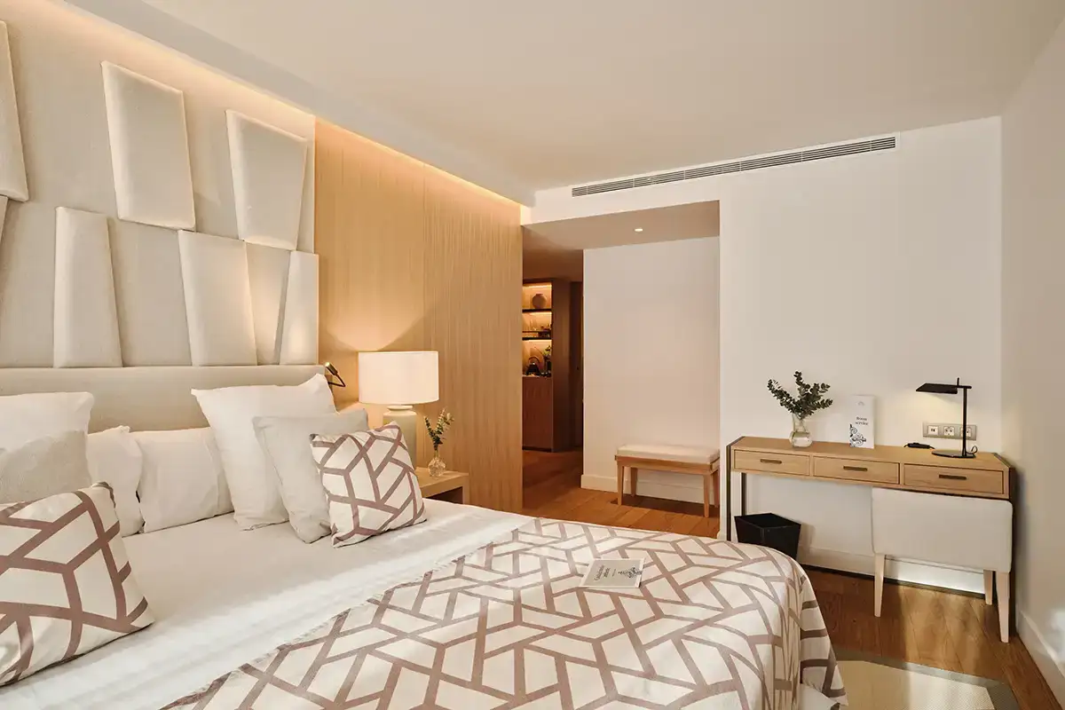 Dormitorio moderno con cama blanca, cabecero y c&oacute;moda con l&aacute;mpara y flores