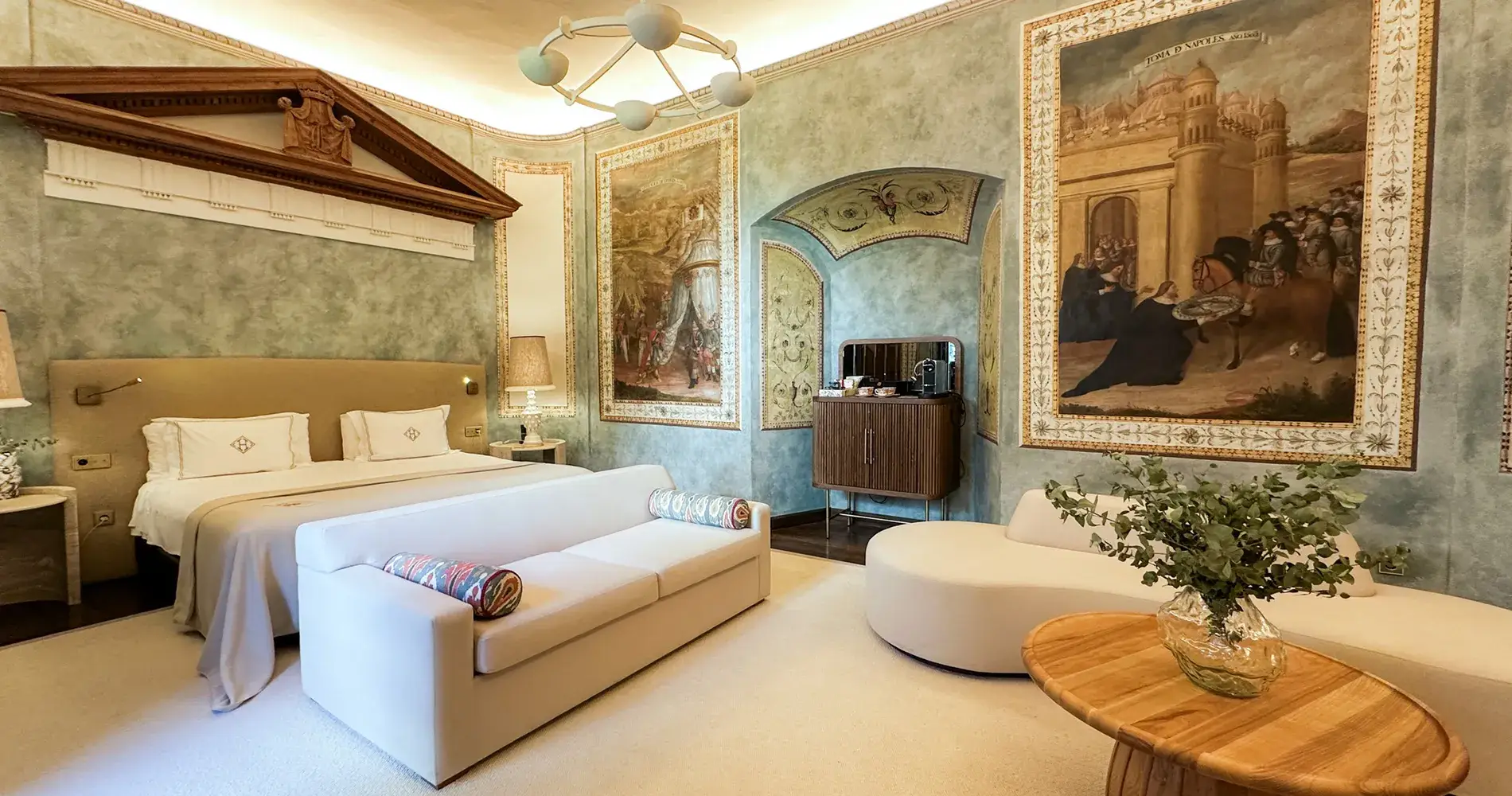 Suite con cama blanca, sof&aacute;, l&aacute;mpara y murales decorativos en la pared