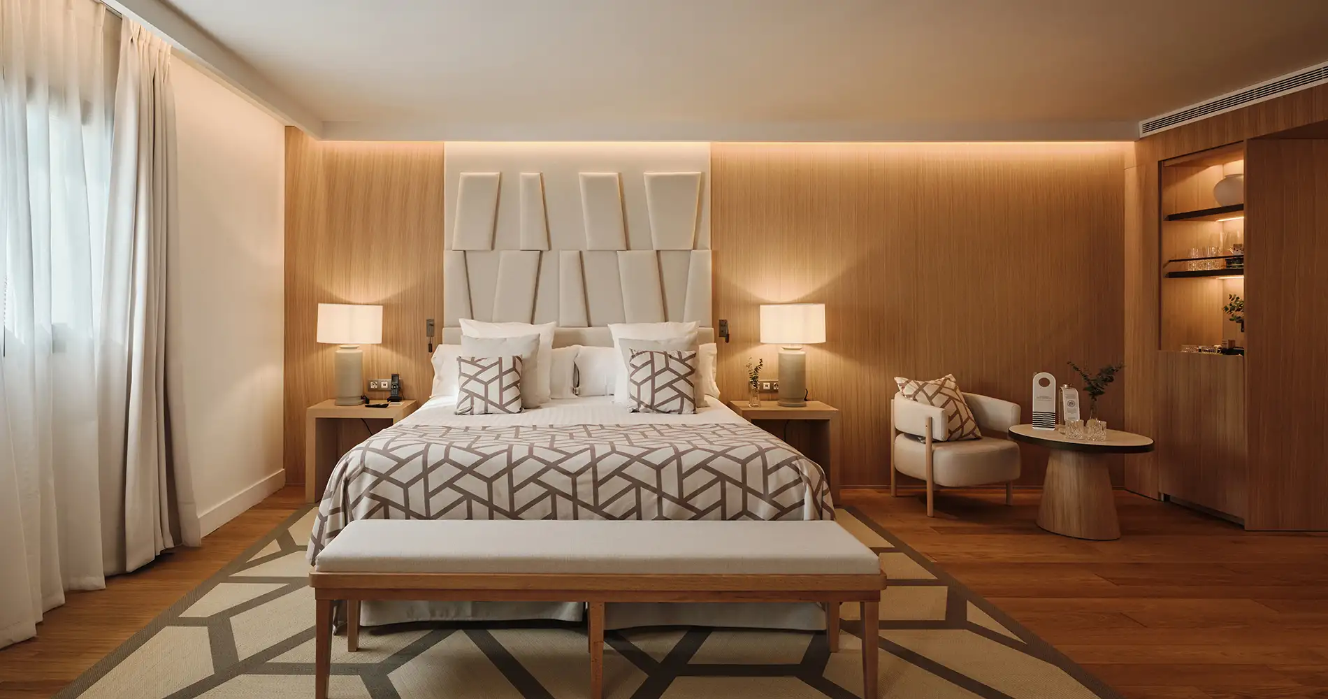Habitaci&oacute;n de hotel moderna con cama, cabecero acolchado y l&aacute;mparas decorativas