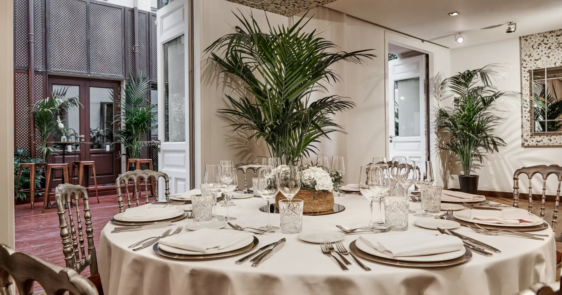 Mesa servida con copas y plantas en un sal&oacute;n luminoso.