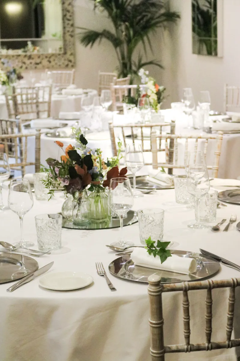Mesa de banquete con cristaler&iacute;a, flores y sillas doradas en un evento.