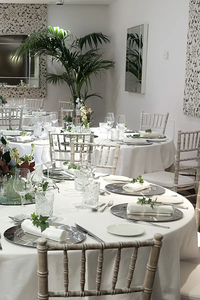 Mesa con manteles blancos y decoraci&oacute;n floral en evento en interior.