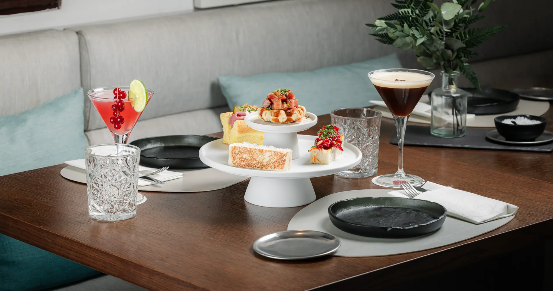 Mesa servida con postre y c&oacute;ctel en sala con sof&aacute;s azules