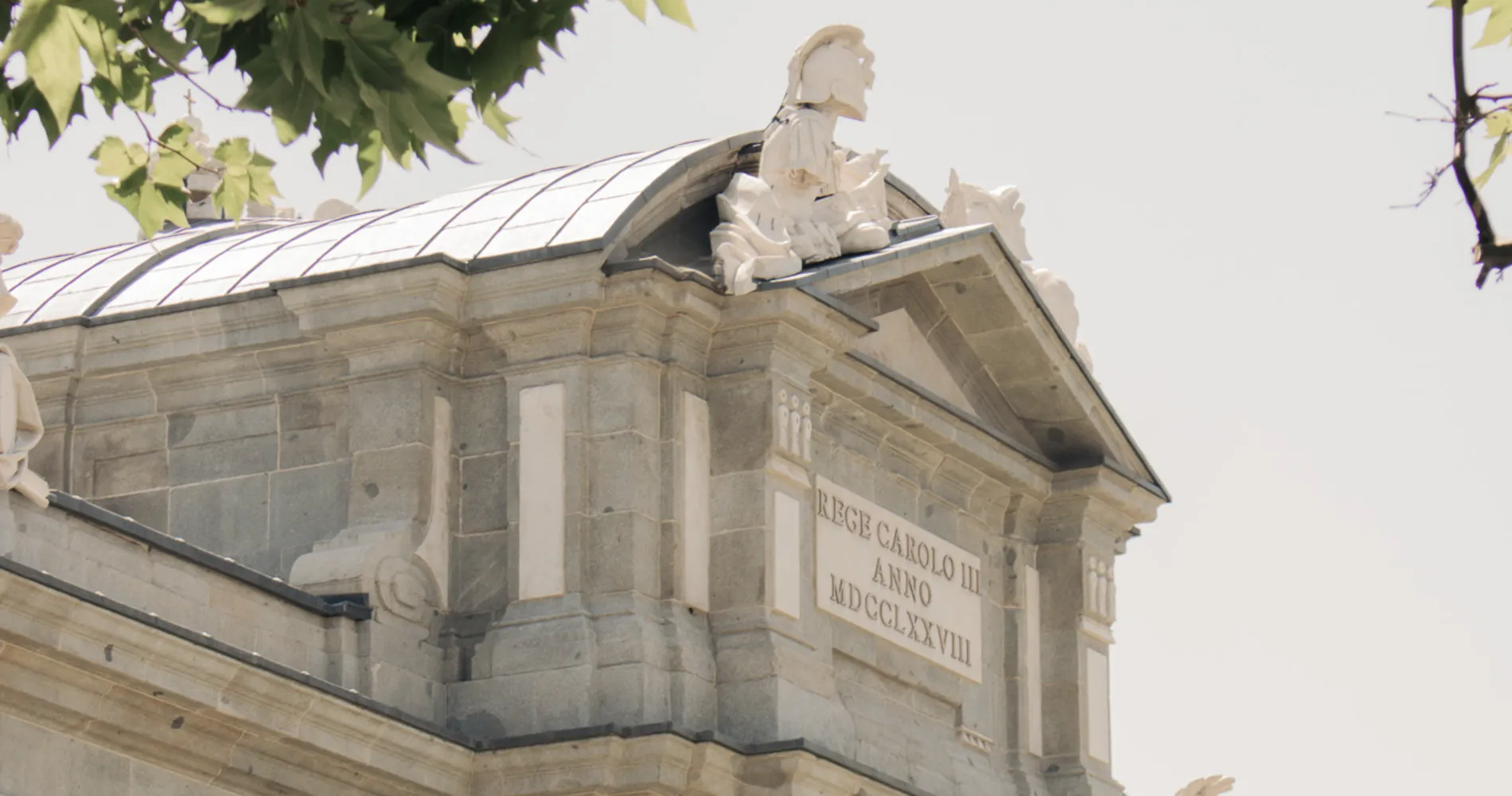 Estatua sobre la fachada de un edificio de piedra con ramas cerca
