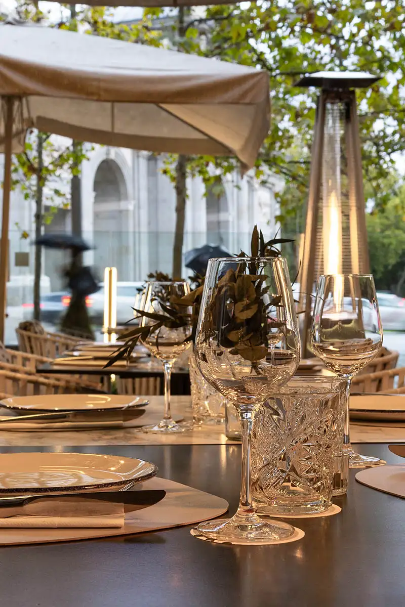 Mesa de banquete al aire libre con copas de vino y luces bajo carpa.