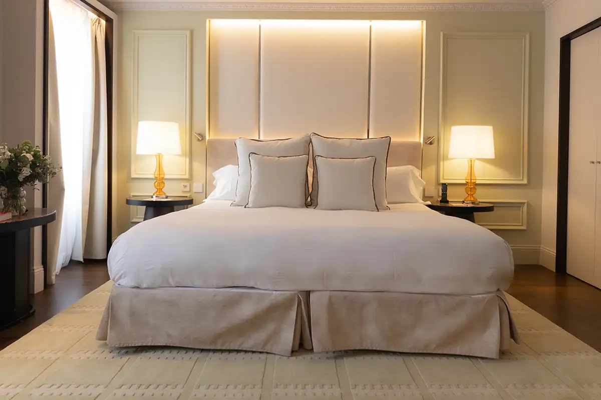 Dormitorio elegante con cama blanca, almohadas grises y l&aacute;mparas de noche.