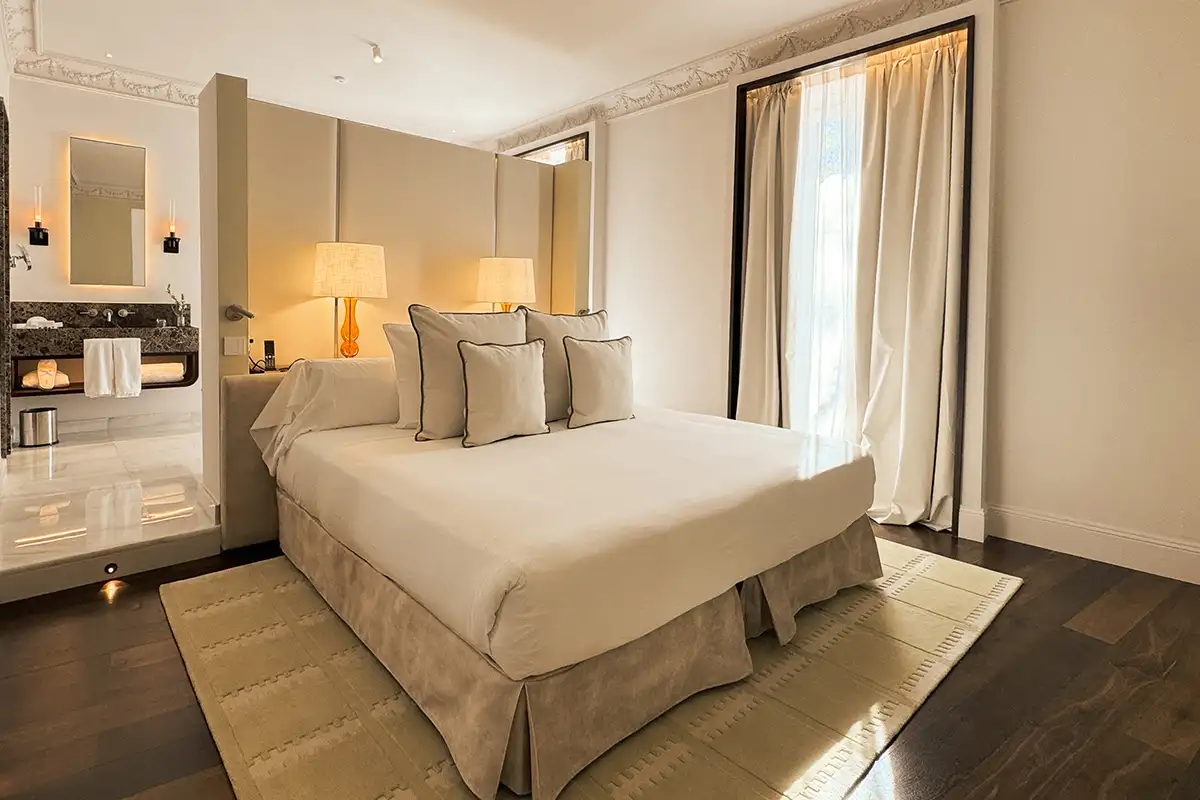 Dormitorio elegante con cama blanca, almohadas y cortinas junto a ventanal
