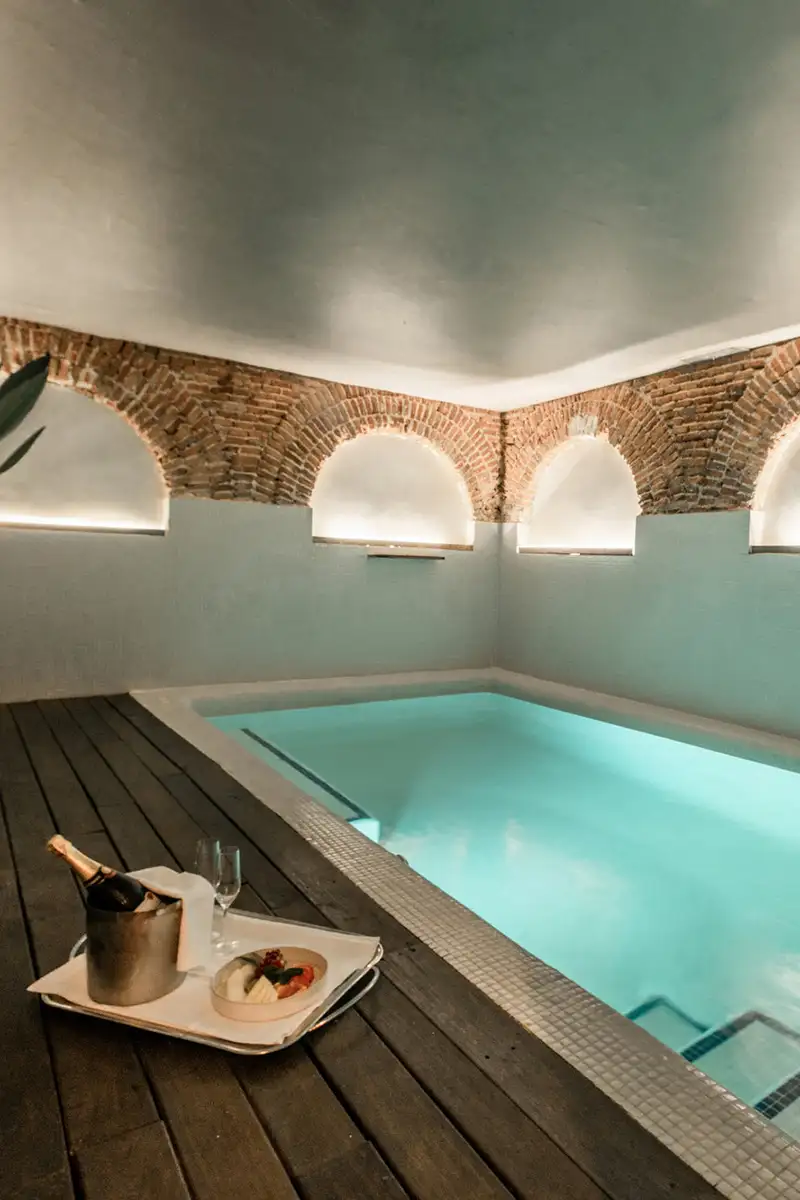 Piscina interior con azulejos, arcos de ladrillo y mesa con bebidas