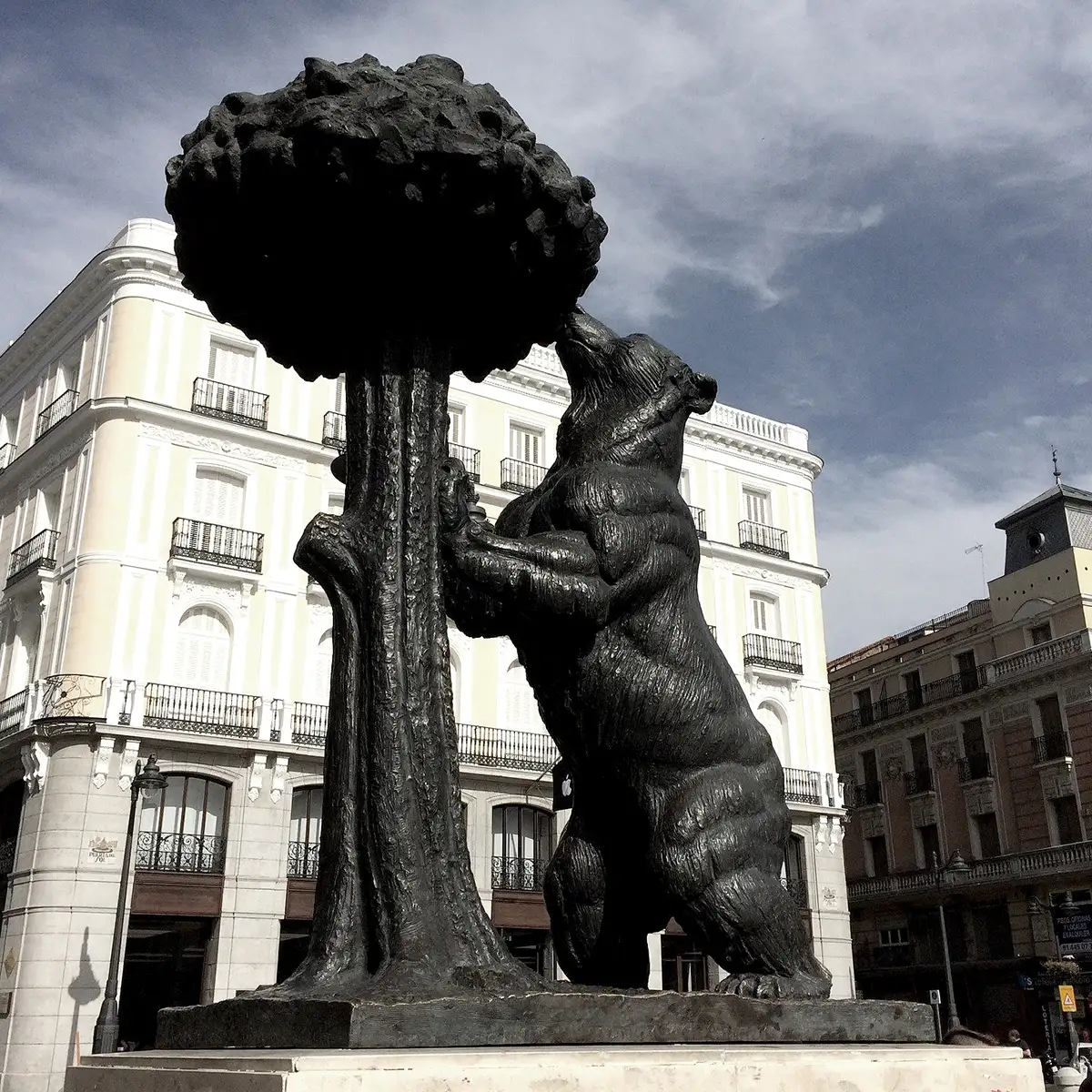 Estatua de bronce de un ni&ntilde;o cargando uvas, frente a edificios.