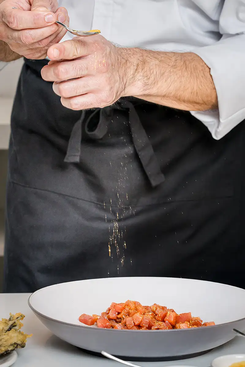 Manos de un cocinero salteando con cuchara, sirve un plato de tomate picado