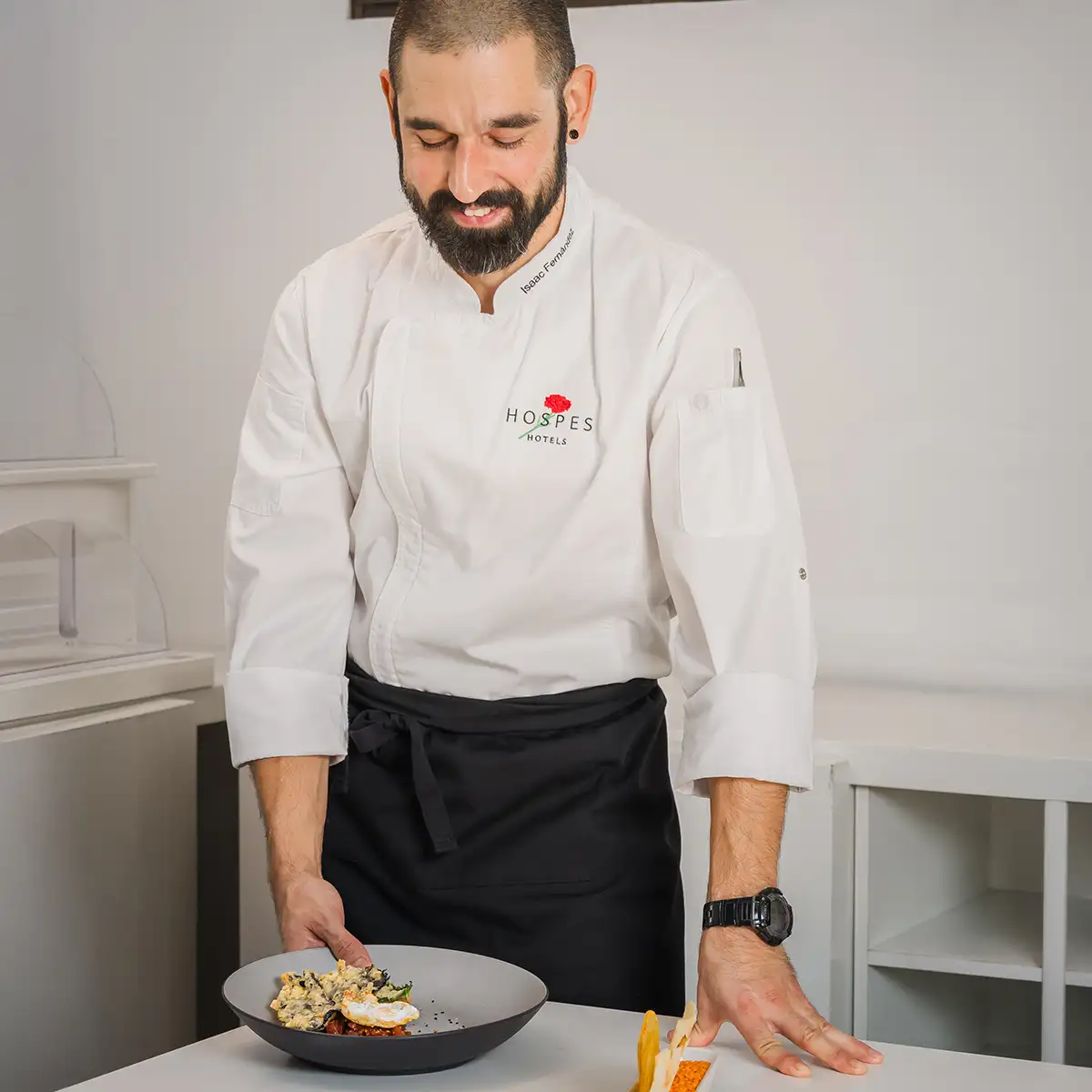 Chef con uniforme blanco sirviendo un plato en cocina blanca