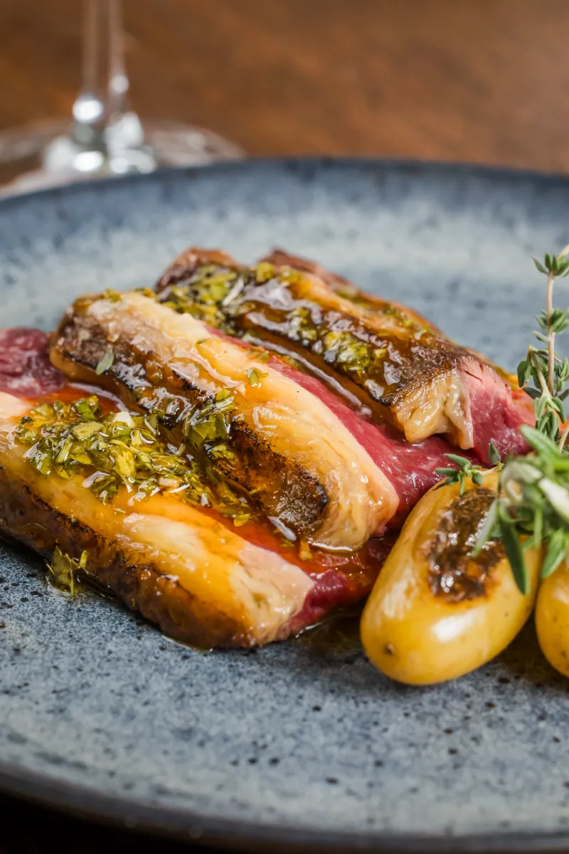 Asado de carne con salsa, hierbas y tomates peque&ntilde;os en plato de piedra