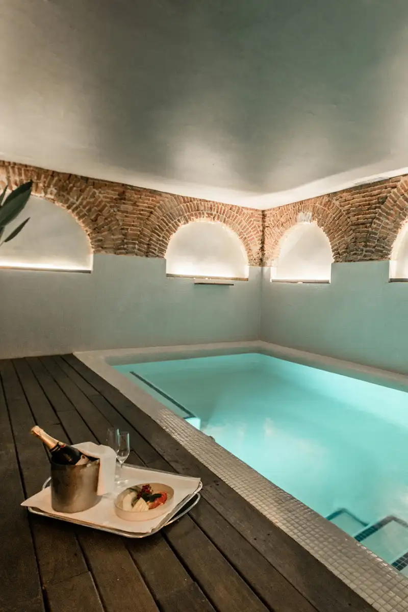 Piscina interior con arcos de ladrillo y bandeja servida en terraza de madera