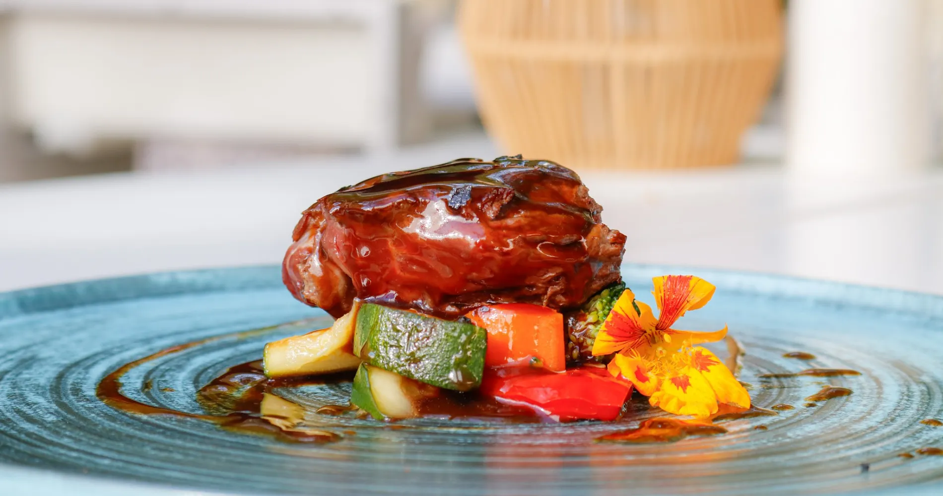 Carne asada con verduras y flor comestible en plato, primer plano