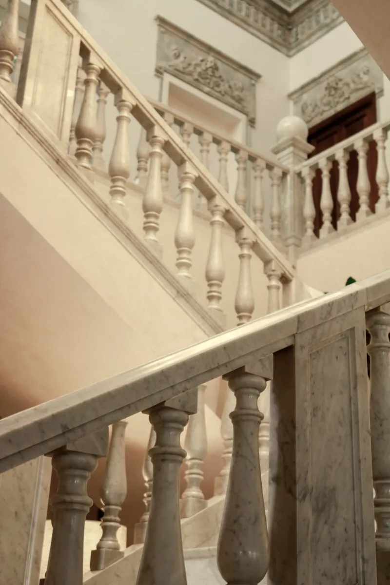 Escalera interior con barandales tallados y columnas decorativas, vista desde abajo