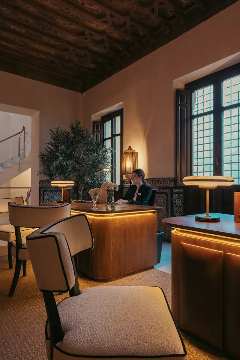Oficina elegante con recepcionista, ventanales y l&aacute;mparas de luz c&aacute;lida.