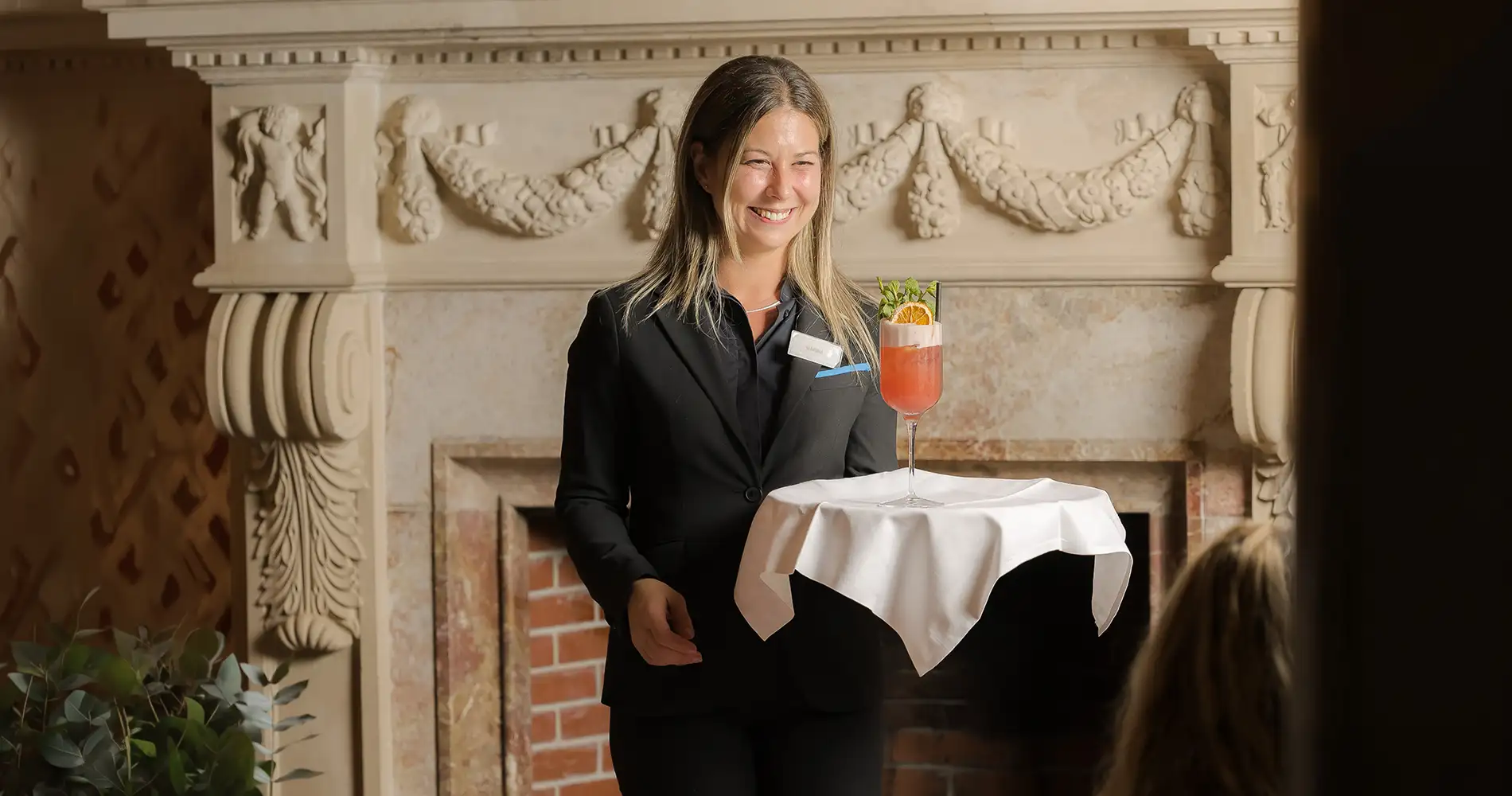 Recepcionista con copa de c&oacute;ctel en un sal&oacute;n decorado con chimenea