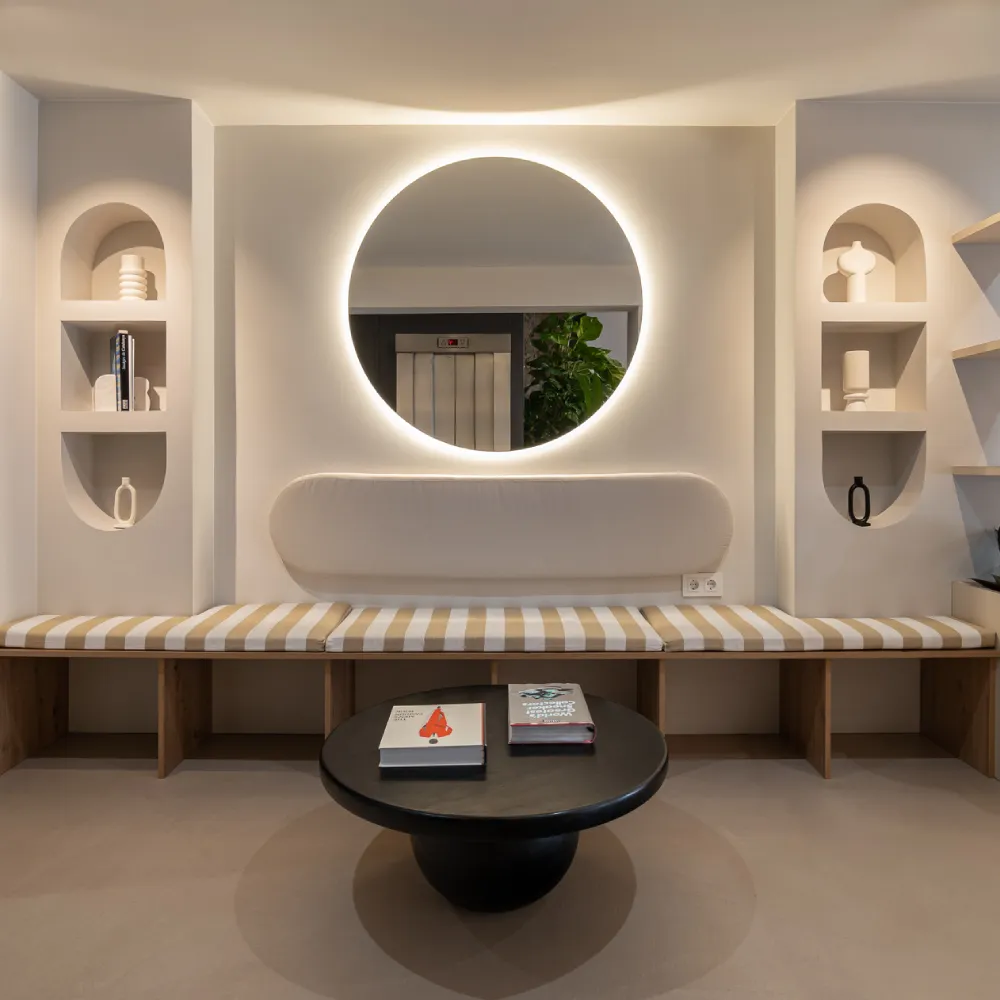Sala moderna con espejo circular iluminado y muebles minimalistas.