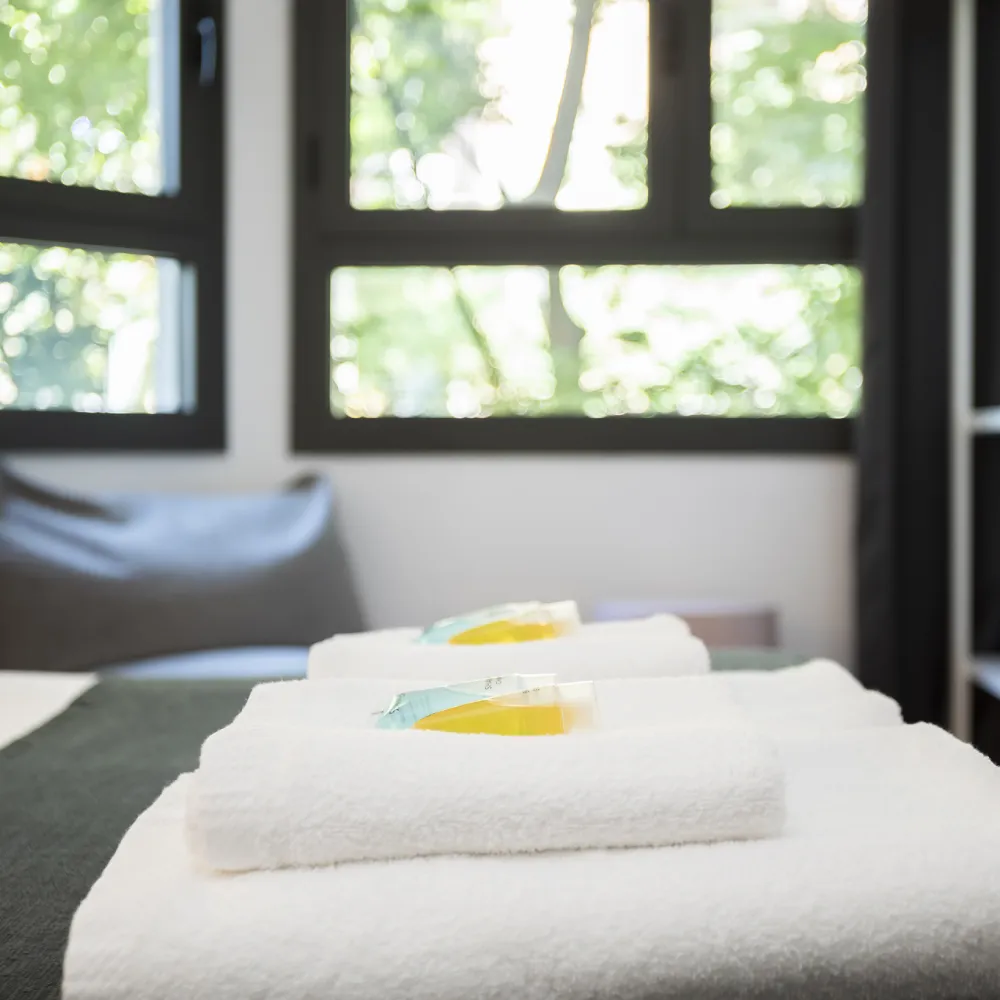Toallas blancas dobladas con art&iacute;culos de tocador, junto a una ventana.