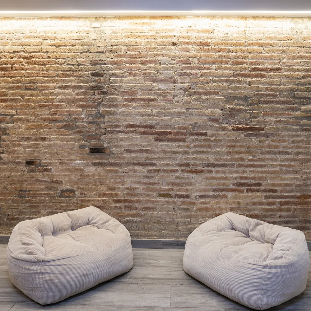 Dos puffs beige frente a una pared de ladrillo.