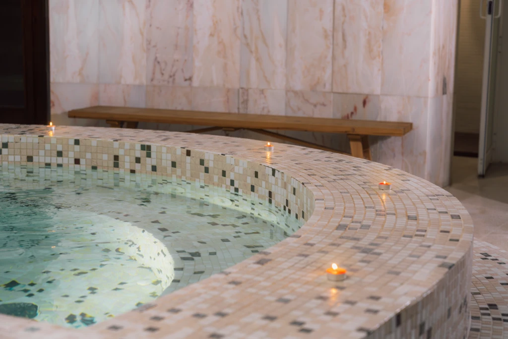Piscina interior con azulejos, borde curvo e iluminaci&oacute;n con velas flotantes