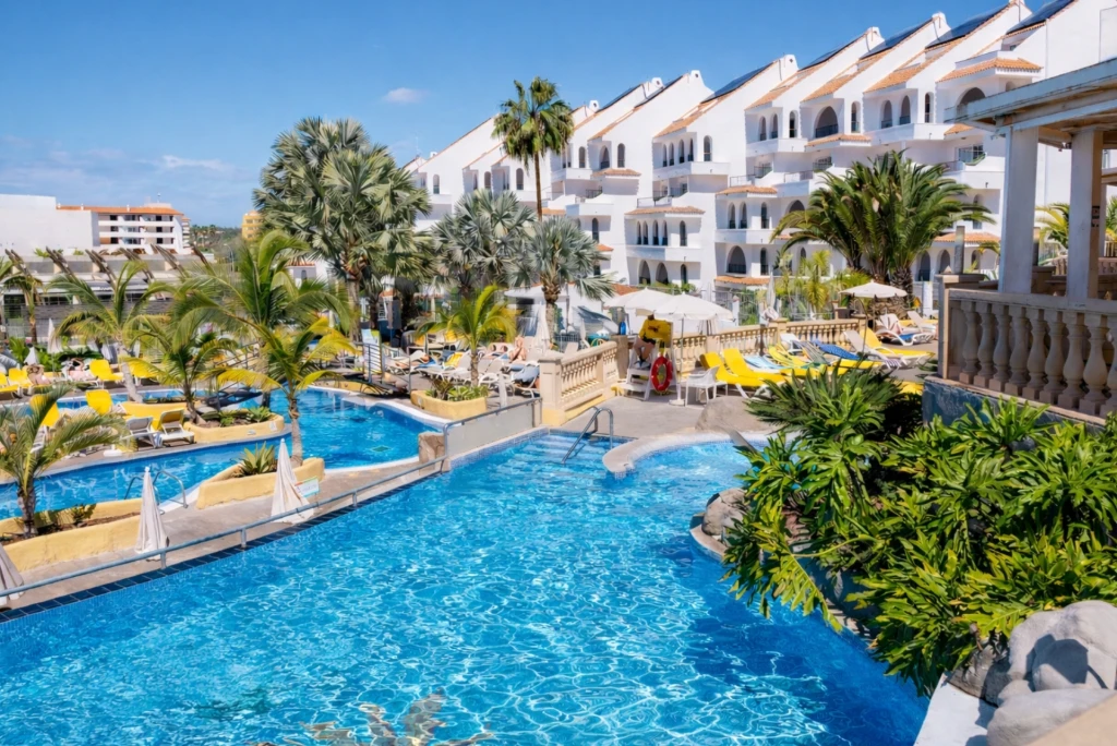 Piscina azul con palmeras y complejo hotelero blanco al fondo