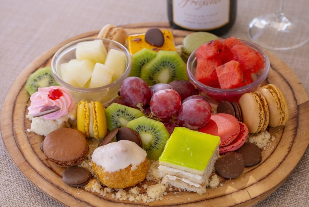 Bandeja de postres variados con frutas y macarons sobre mesa de madera