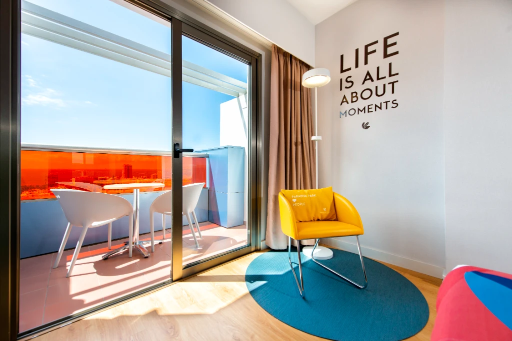 Sala moderna con sill&oacute;n amarillo, luz y acceso a terraza con mesa.