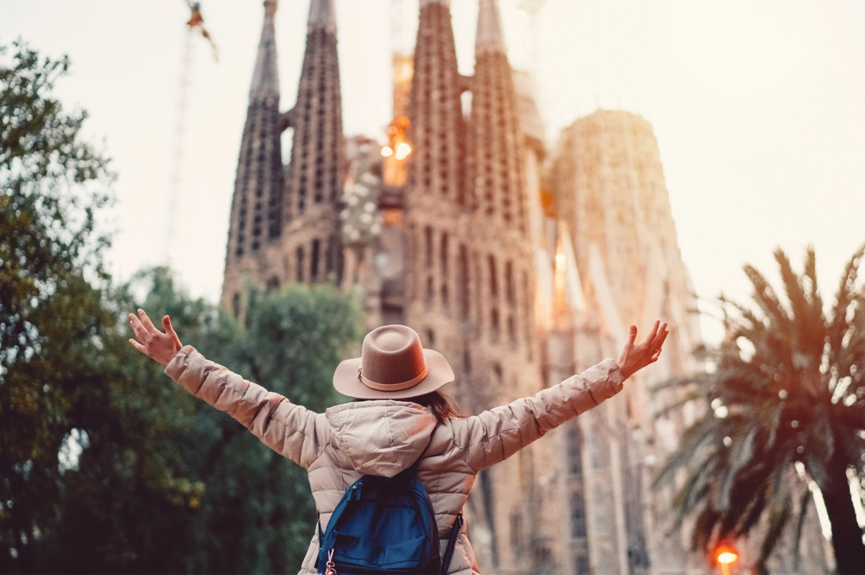 Traveler with arms raised admiring the Sagrada Familia in Barcelona at sunset.