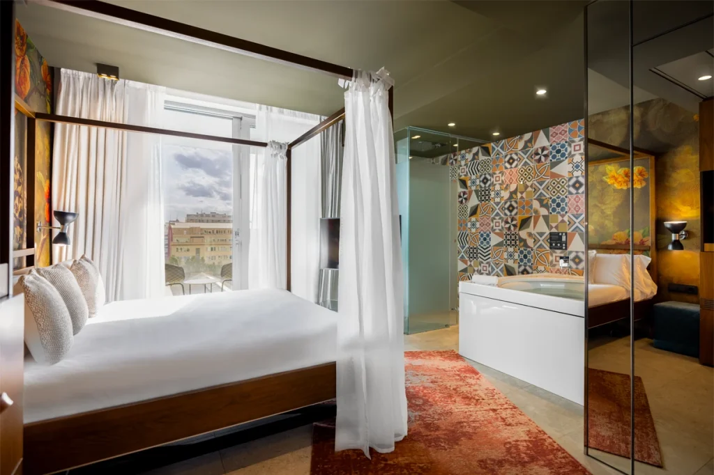 A stylish modern hotel room featuring a four-poster bed and vibrant patterned wall.