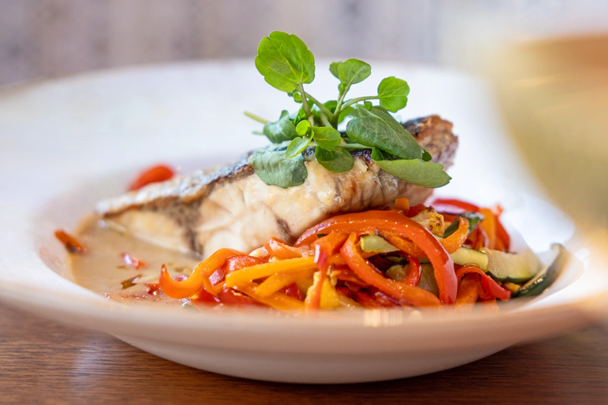 A delicious plate of grilled fish served with colorful saut&eacute;ed vegetables.