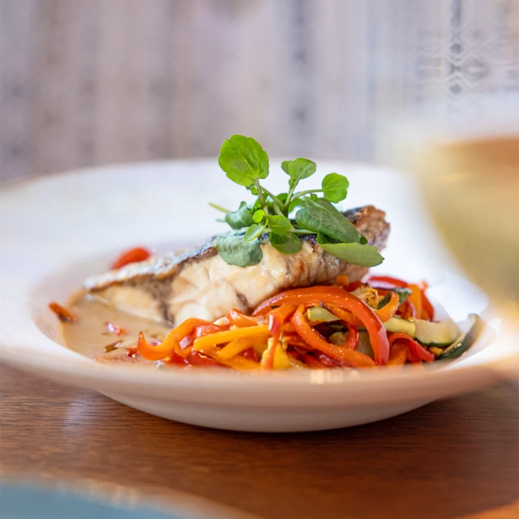 A delicious plate of grilled fish served with colorful saut&eacute;ed vegetables.