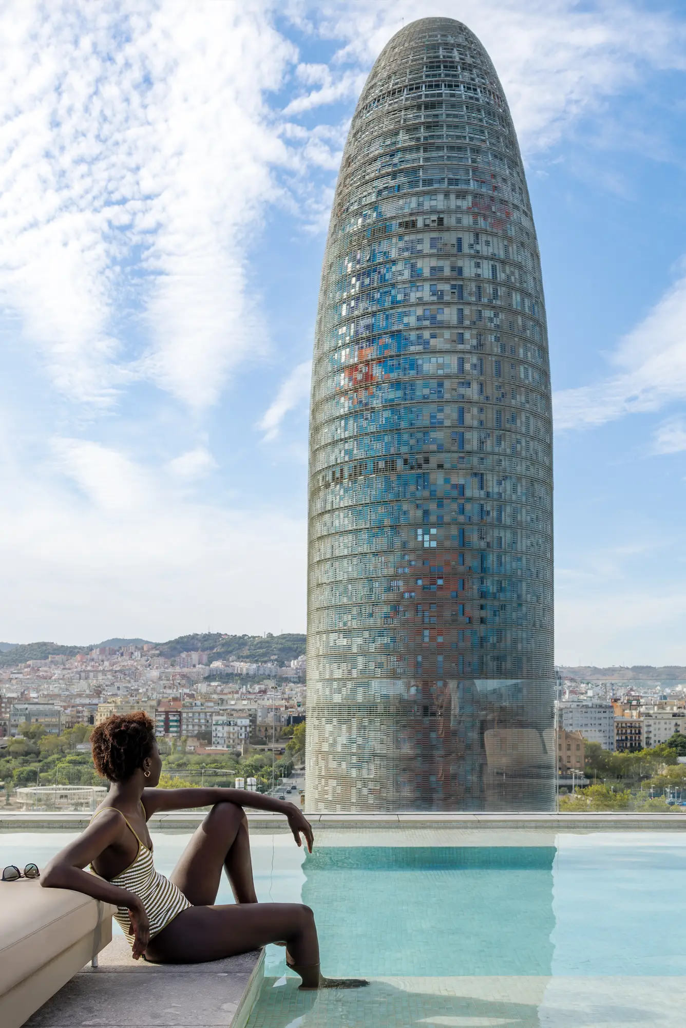 A woman relaxing by the pool with views of the Barcelona skyline and Torre Gl&ograve;ries
