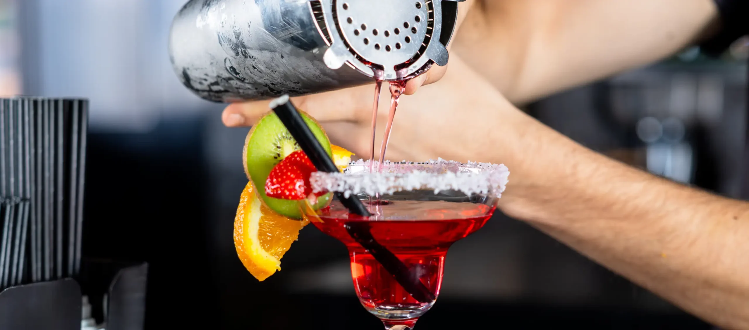 Bartender pouring a cocktail into a glass with garnishes
