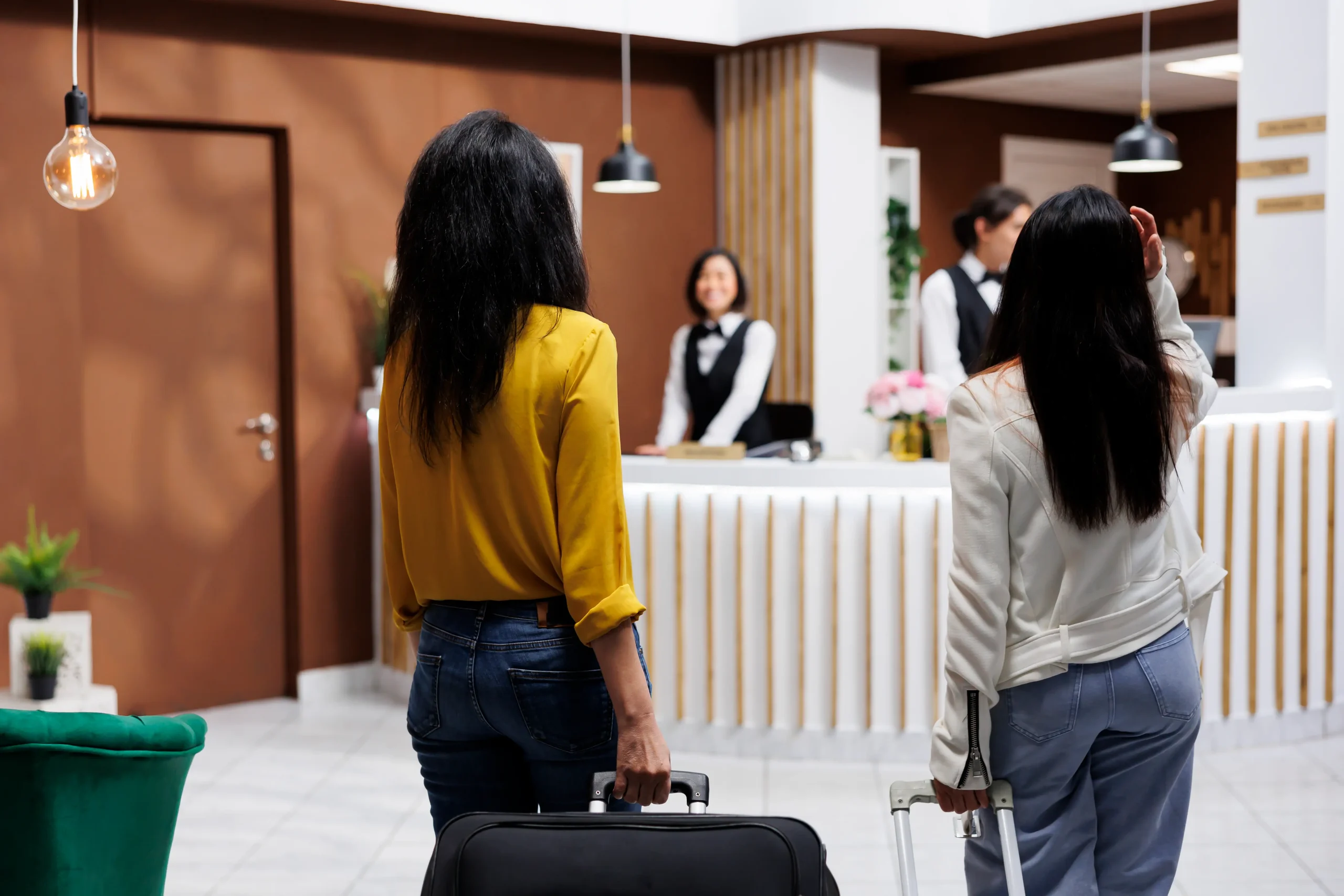 Dos mujeres con maletas hablando con recepcionistas en el lobby de un hotel.