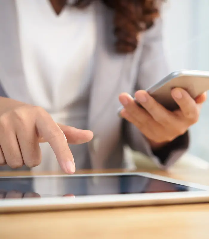 Persona usando smartphone y tableta simult&aacute;neamente sobre una mesa de madera.