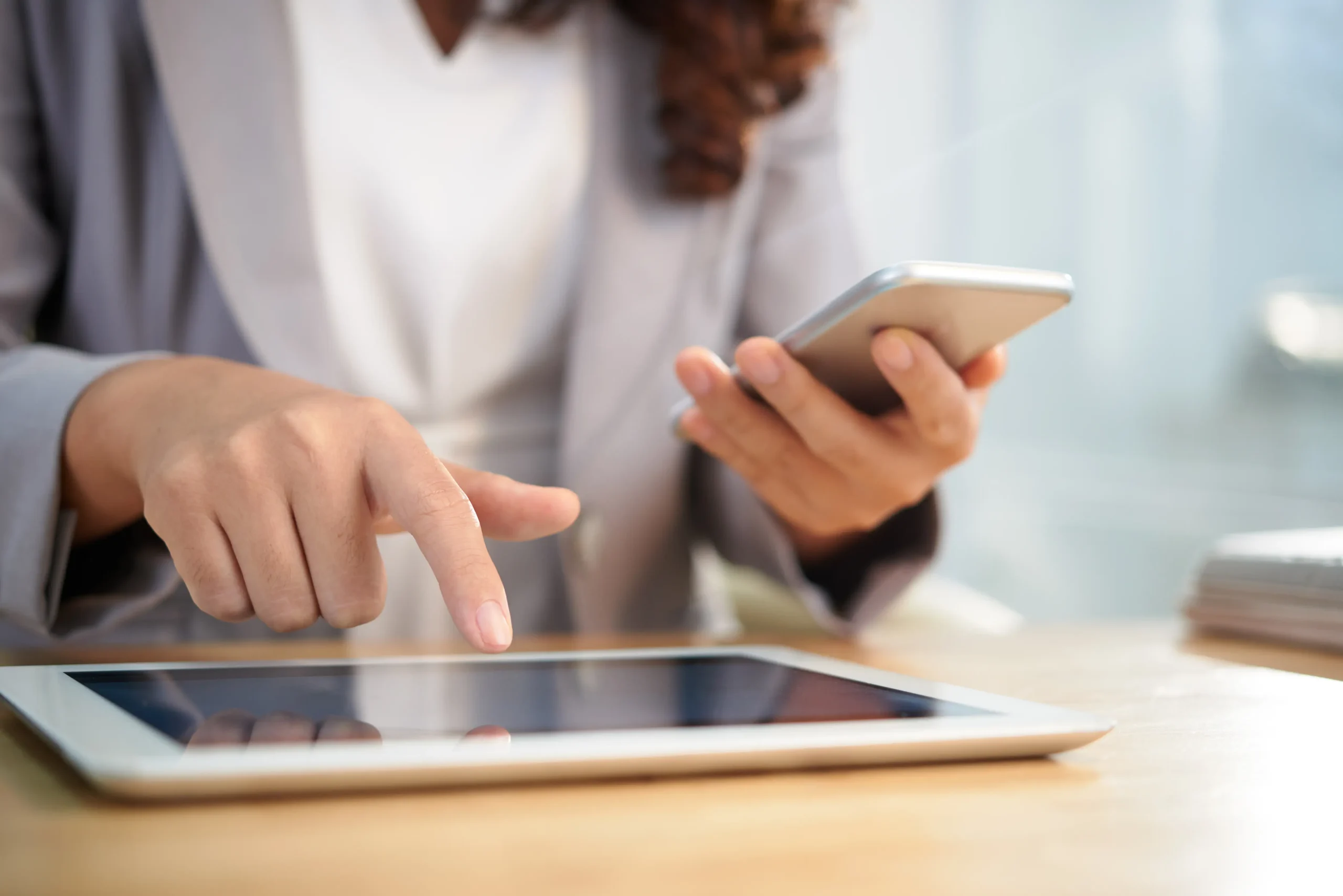 Mujer usando tablet y sosteniendo un smartphone en oficina.