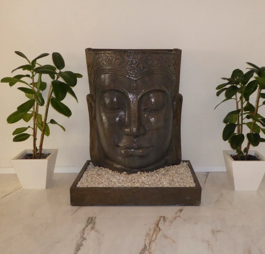 Estatua de rostro sereno entre dos macetas con plantas verdes.